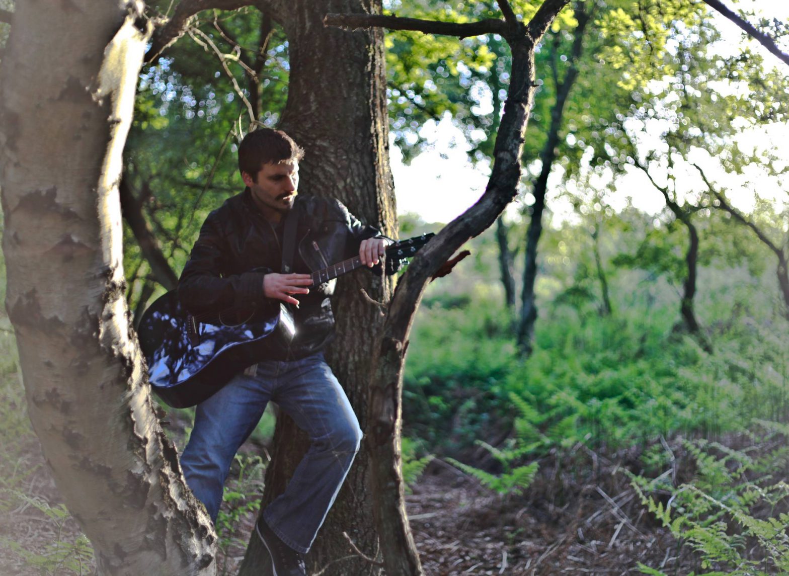 photo of a man on his guitar in a forest
